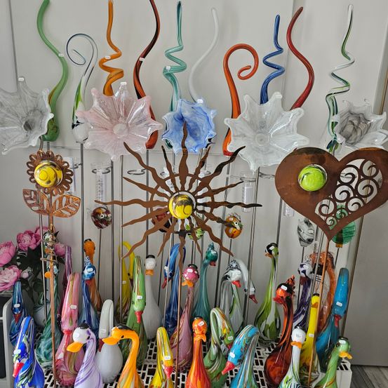 Eine Ausstellung bunter Glasfiguren, darunter Blumen, Schwäne und andere abstrakte Formen, mit verschiedenen Größen und lebendigen Farben, vor weißem Hintergrund.