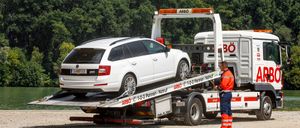 Ein weißes Auto wird von einem Abschleppwagen abtransportiert. Der Lastwagen hat ein Nummernschild, das ARBO liest. Das Auto hat ein Nummernschild, das L 667 LS liest.
