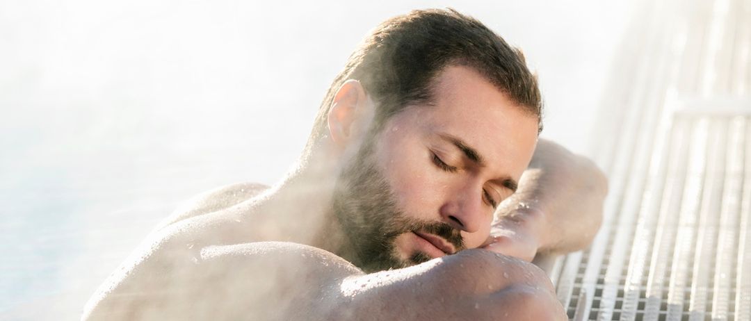 Ein bärtiger Mann ruht im Whirlpool, die Augen geschlossen, mit aufsteigendem Dampf um ihn herum.