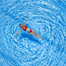 Eine Frau schwimmt im Pool und streckt ihre Arme aus, wodurch eine Welle in dem blauen Wasser entsteht.