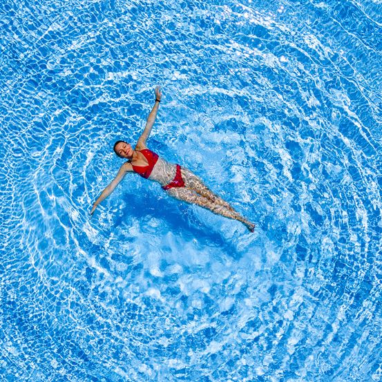 Eine Frau schwimmt im Pool und streckt ihre Arme aus, wodurch eine Welle in dem blauen Wasser entsteht.