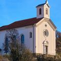 Die weiße Kirche mit einem braunen Dach und einem Turm oben hat ein Kreuzzeichen und eine Uhr auf ihrem Turm.