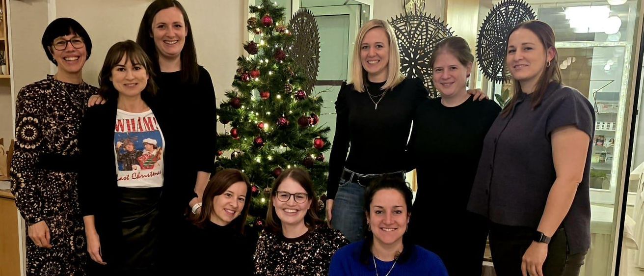 A group of women posing for a photo in front of a decorated Christmas tree in a room.