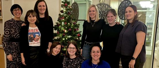 Eine Gruppe von Frauen posiert vor einem geschmückten Weihnachtsbaum in einem Raum.