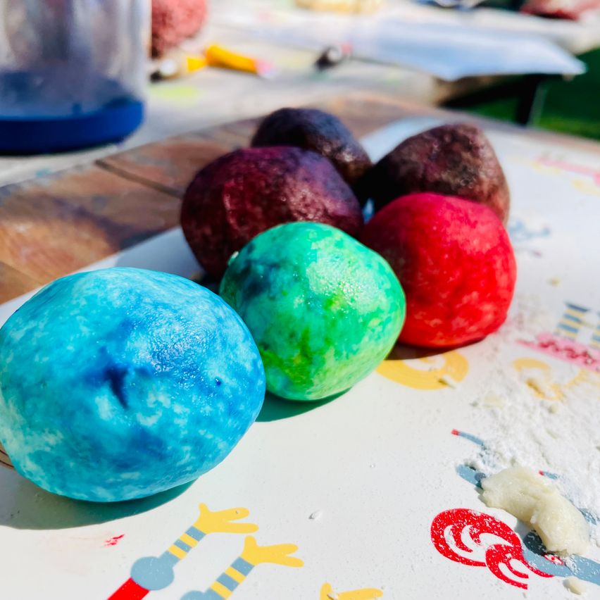 Bunte Ostereier, blau, grün, rot und lila, liegen auf einem Tisch mit Malutensilien.