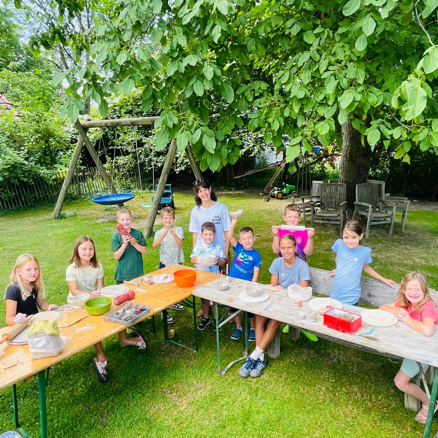 Kinder und Betreuerin bei einem Töpferkurs im Freien in einem Garten mit Schaukel