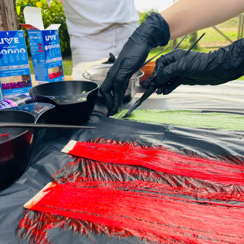 Haare färben: rote und grüne Strähnen auf schwarzer Unterlage mit schwarzen Handschuhen