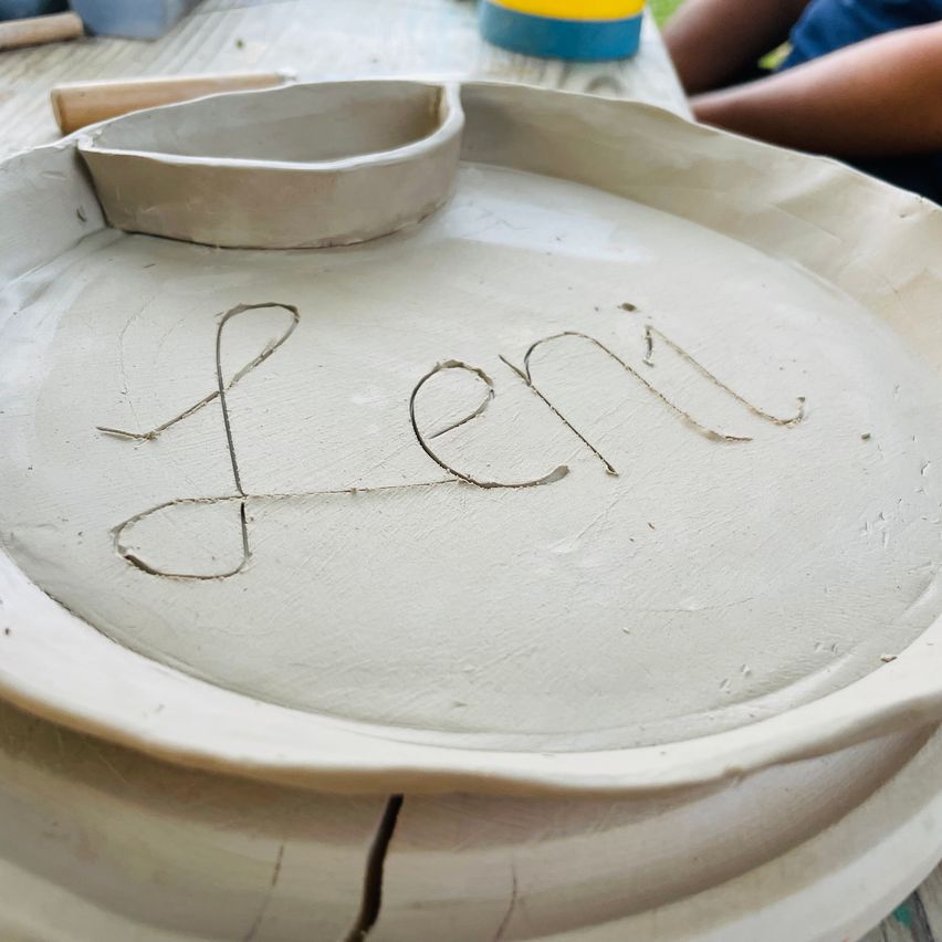 Eine weiße Keramikplatte mit dem Namen 'Len' in kursiver Schrift darauf. Eine kleine Keramikschale liegt auf der Platte.