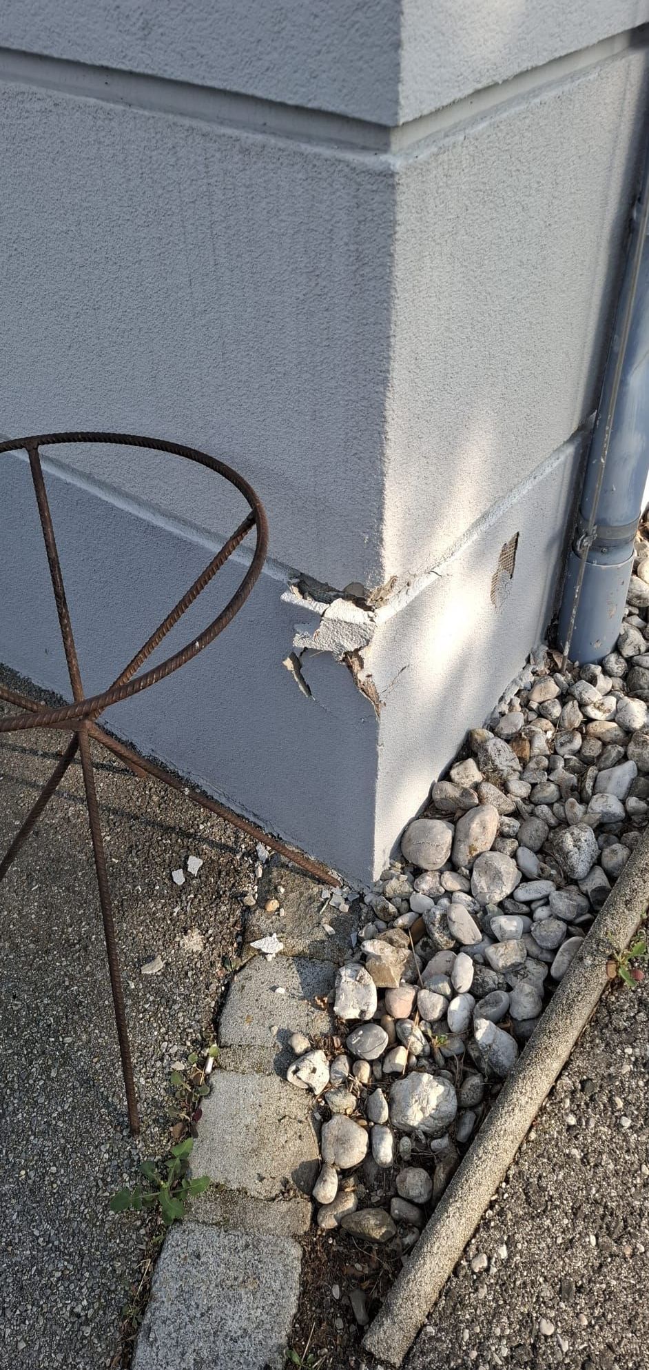 Nahaufnahme einer verwitterten Wandecke mit abblätternder Farbe und einem rostigen Metallständer in der Nähe.