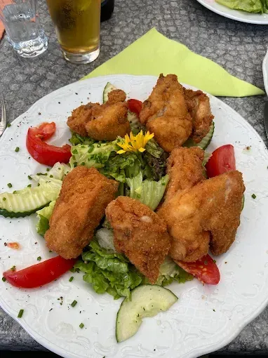 Ein weißer Teller mit gebratenem Hühnchen, Salat und Tomaten auf einem Tisch. Glas Bier und Glas Wasser in der Nähe.