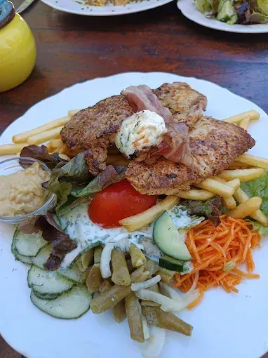 Ein Teller mit Fleisch, Pommes, Salat und Gemüse auf einem Holztisch.