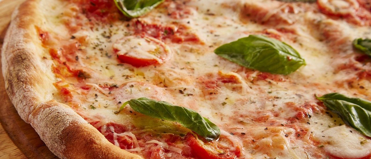 Ein Nahaufnahme einer Pizza mit geschmolzenem Käse, frischen Basilikumblättern und geschnittenen Tomaten auf einer Holzoberfläche.