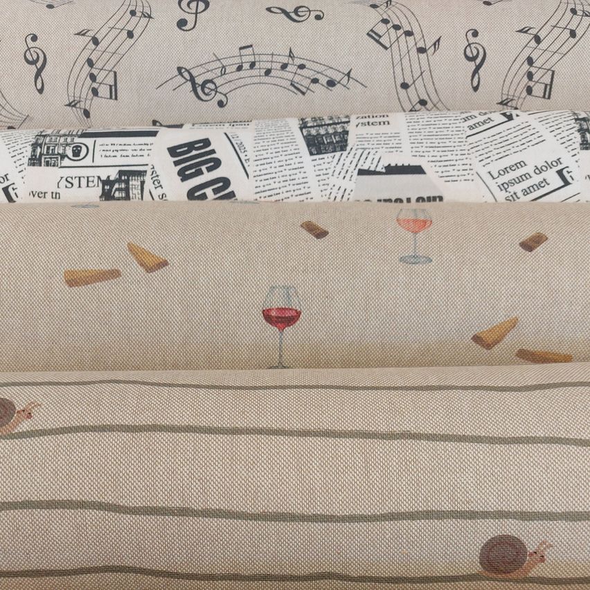 A stack of fabric rolls with different patterns: music notes, newspaper clippings, wine glasses, and a snail.