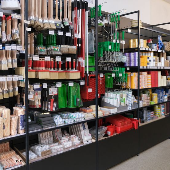 Ein Geschäft mit Regalen, die verschiedene Werkzeuge wie Pinsel, Walzen und Aufbewahrungsbehälter in verschiedenen Farben und Typen präsentieren.