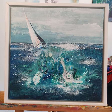 Ein gerahmtes Gemälde eines Segelboots im Ozean mit spritzenden Wellen. Das Gemälde hat einen modernen Kunststil mit einer Mischung aus blauen, grünen und weißen Farben. Der Rahmen ist weiß mit einem leicht erhöhten Rand.