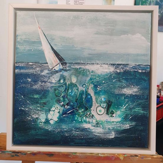 Ein gerahmtes Gemälde eines Segelboots im Ozean mit spritzenden Wellen. Das Gemälde hat einen modernen Kunststil mit einer Mischung aus blauen, grünen und weißen Farben. Der Rahmen ist weiß mit einem leicht erhöhten Rand.