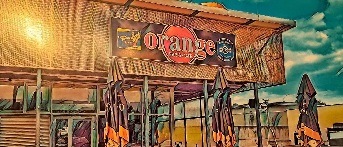 Ein Außenbereich des Orange Bar & Cafe mit orangefarbenen Stühlen, Tischen und Schirmen. Das Schild sagt Orange Bar & Cafe.