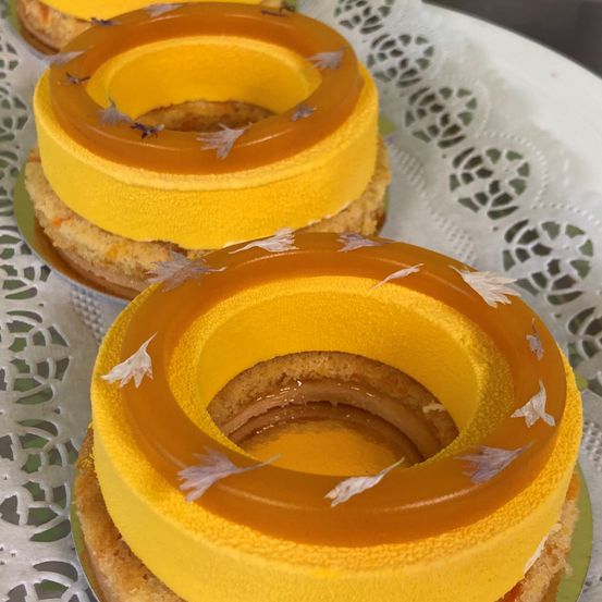 Eine Nahaufnahme von zwei golden glasierten Kuchen auf einem weißen Doily. Die Kuchen haben ein Spiraldesign mit gelber Glasur und weißen Federdekorationen.