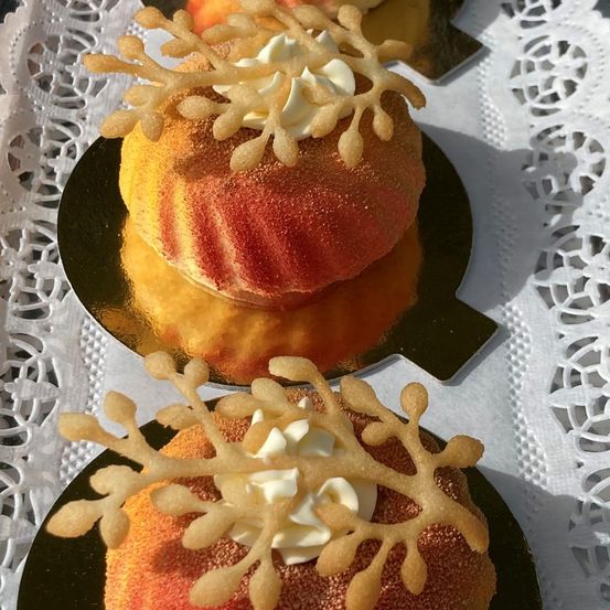 Drei Desserts auf goldenen Tellern, verziert mit weißer Sahne und schneekellochenartigen Dekorationen, auf einem weißen Spitzentuch platziert.