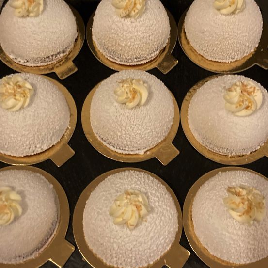 Ein Nahaufnahme von mehreren weißen Desserts, die mit Sahne gekrönt und mit gelben Blumen auf goldenen Tellern dekoriert sind, vor einem schwarzen Hintergrund.