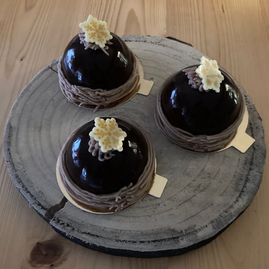 Drei Schokoladendesserts mit weißen Schneeflocken-Designs auf einem Holztisch, auf einem grauen runden Teller platziert.