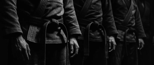 Ein Schwarz-Weiß-Foto zeigt Kampfkünstler in traditionellen Uniformen, die Seite an Seite stehen und sich auf ihre Gürtel konzentrieren.