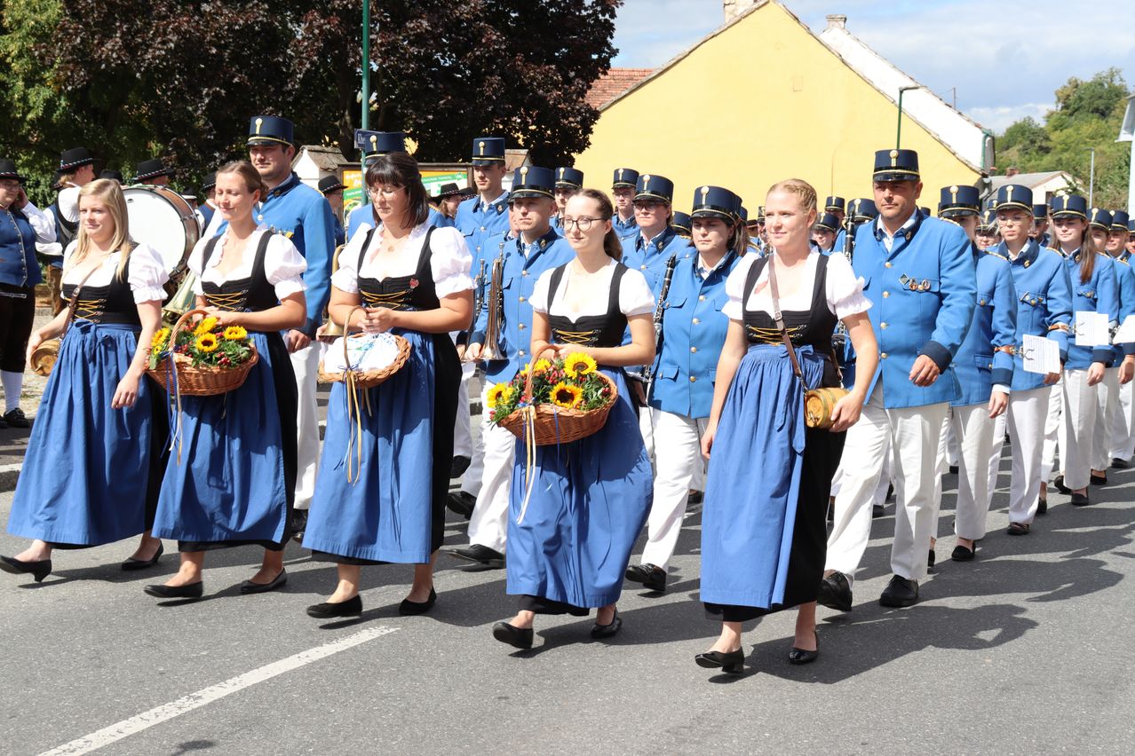 Eine Gruppe von Frauen in traditionellen blauen Kleidern und Männern in blauen Uniformen mit Hüten marschiert bei einer Parade mit Blumenkörben.