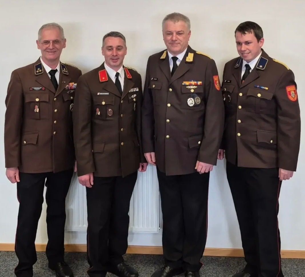 Vier Männer in Militäruniformen stehen zusammen und lächeln. Sie stehen vor einer weißen Wand.