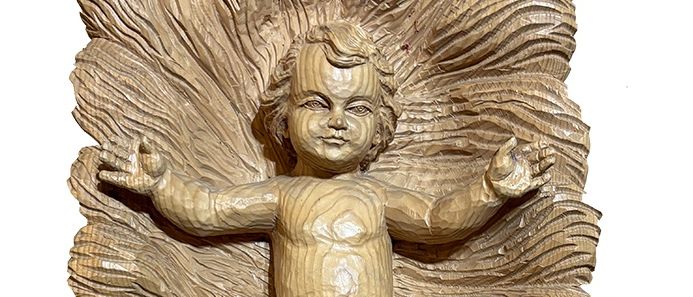 Eine Holzskulptur eines Babys, sitzend auf einer gebogenen, strukturierten Oberfläche, mit einem kleinen Gewand, einem ruhigen Gesichtsausdruck und offenen Armen.