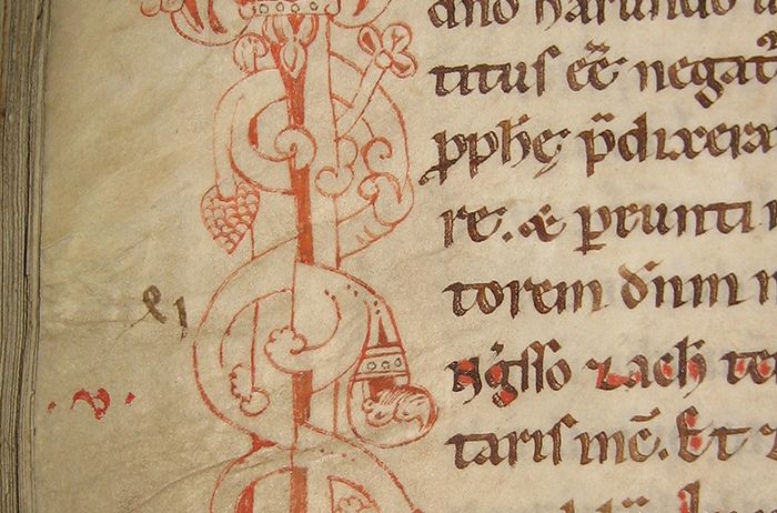 Eine gealterte Manuskriptseite mit komplizierten mittelalterlichen Illustrationen und handgeschriebenem Text in roter Tinte. Die Illustrationen umfassen einen zentralen Stab mit floralen Motiven und einer Krone.