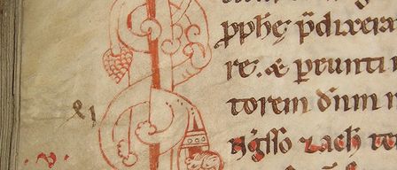 Eine gealterte Manuskriptseite mit komplizierten mittelalterlichen Illustrationen und handgeschriebenem Text in roter Tinte. Die Illustrationen umfassen einen zentralen Stab mit floralen Motiven und einer Krone.