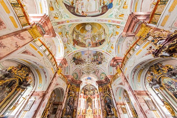 Einfache Fresken zieren die hohe Decke und Bögen einer Kirche, mit goldenen Akzenten und detaillierten biblischen Szenen.