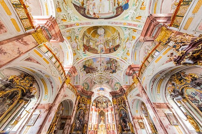 Das Innere einer Barockkirche mit aufwendigen Fresken an der Decke und den Wänden, die religiöse Szenen und goldene Akzente zeigen.