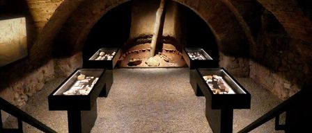 A dimly lit room with stone walls and a wooden pole in the center. Three black display cases with artifacts are placed on the floor.