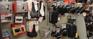 Ein Fahrradzubehörladen präsentiert verschiedene Artikel wie Sättel, Taschen und Lampen. Die Wand ist mit unterschiedlichen Produkten in Schwarz und Weiß gefüllt, ordentlich organisiert.