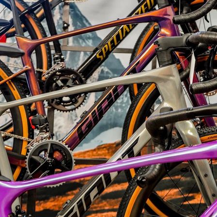 Nahaufnahme mehrerer spezialisierter Fahrräder mit aufwendigen Designs, in den Farben Lila und Silber, vor dem Hintergrund eines Bergrückens.