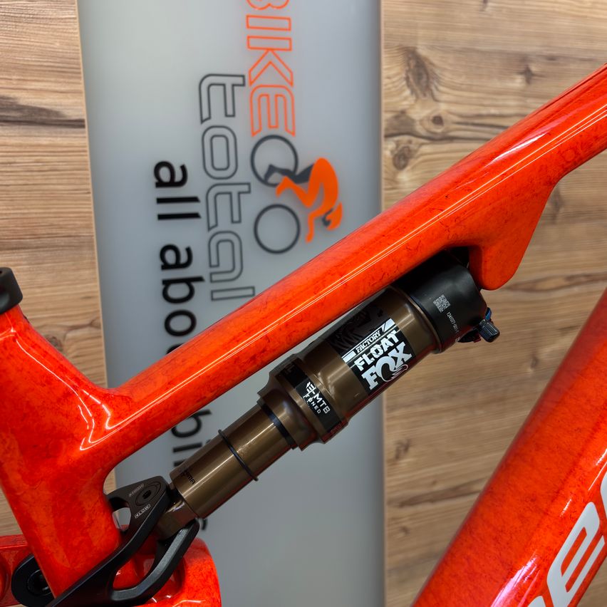Close-up of a vibrant orange bicycle frame featuring a FOX Factory suspension system, set against a wooden background with a 'BIKE QO' logo.