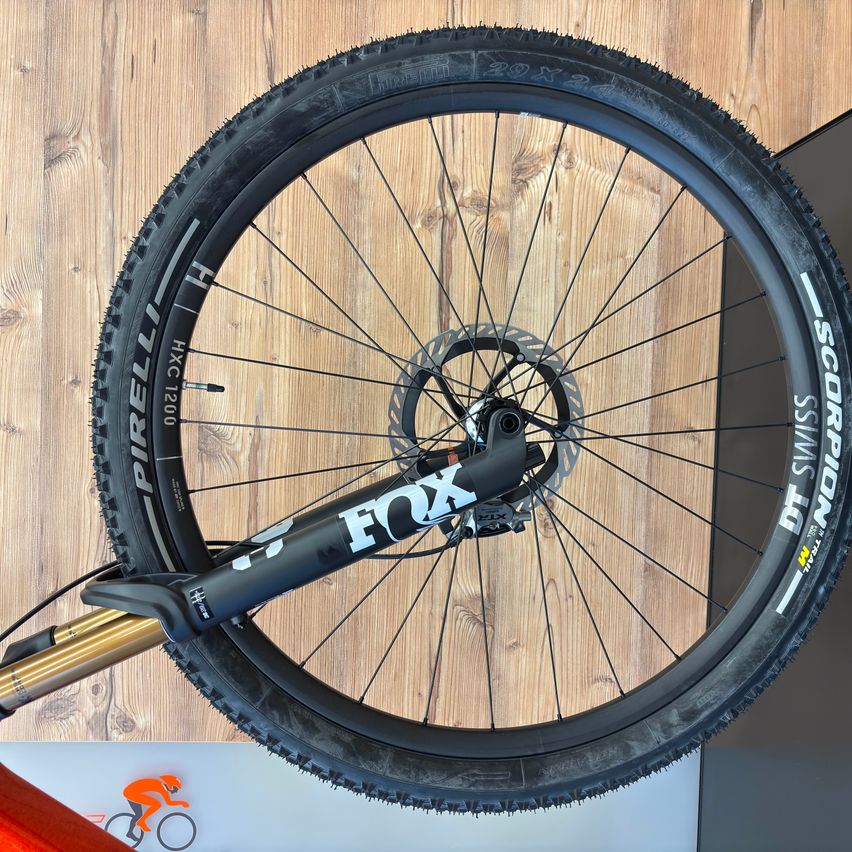 Close-up of a black bicycle wheel, labeled Fox, with Pirelli tires, displayed on a wooden background.