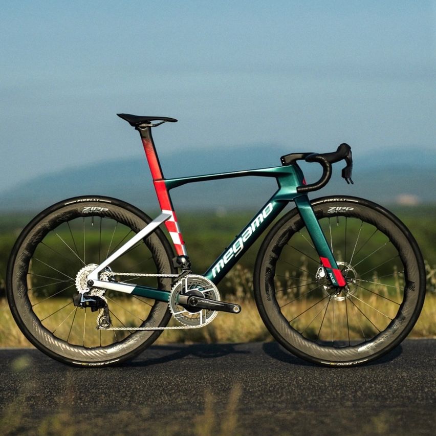 Ein schlankes, grün-rotes Rennrad mit Zipp-Reifen steht auf einer Straße mit einer malerischen Kulisse.