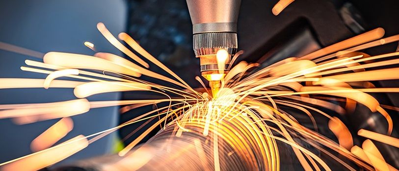 Eine Maschine mit hellem Licht schneidet ein Metallrohr und gibt Funken ab. Der Hintergrund ist dunkel.