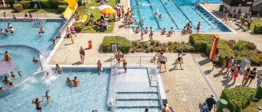 Eine Luftaufnahme eines Freizeitzentrums mit mehreren Schwimmbecken und Wasserrutschen. Viele Menschen genießen das Wasser. Die Saison beginnt am 23. Mai 2026.