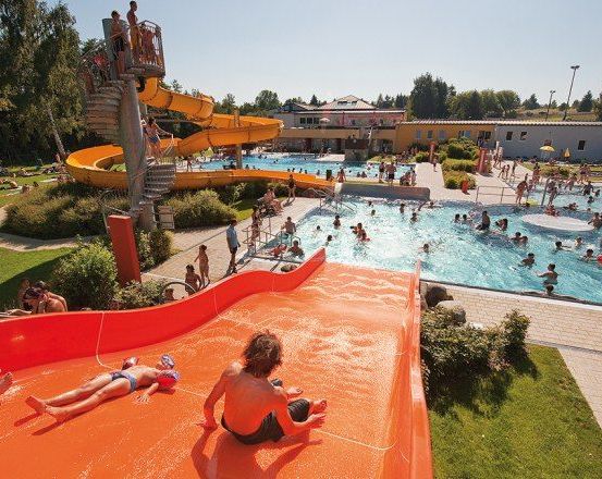 Ein Wasserpark mit Menschen, die im Pool schwimmen, eine gelbe Wasserrutsche hinuntergleiten und an einem sonnigen Tag die Natur genießen.