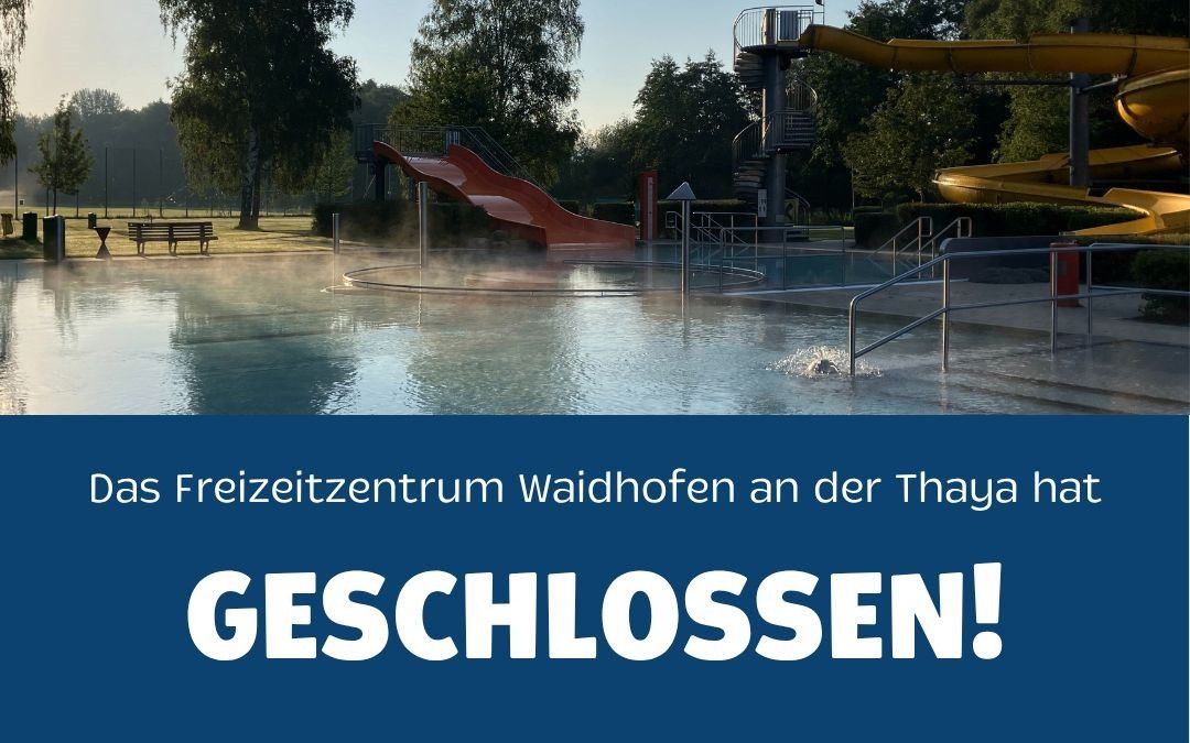 An outdoor pool with a red slide and a yellow slide, surrounded by trees and a bench. The water is calm with a splash, and the sign reads 'Freizeitzentrum Waidhofen an der Thaya Geschlossen!' in white on a blue background.