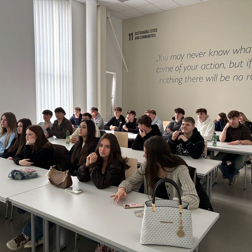 A classroom filled with students attending a lecture. A motivational quote on the wall. Various personal items on desks.