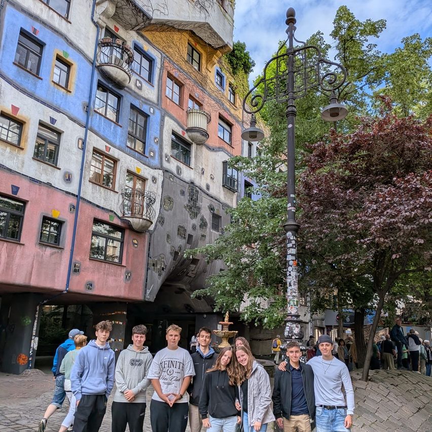 Eine Gruppe junger Leute posiert vor einem bunten, skurrilen Gebäude mit Graffiti und Straßenlaternen.