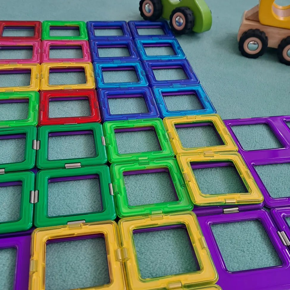 Eine Sammlung bunter, magnetischer Spielsteine auf einem Teppichboden, angeordnet in einem Muster mit Spielzeugfahrzeugen in der Nähe.