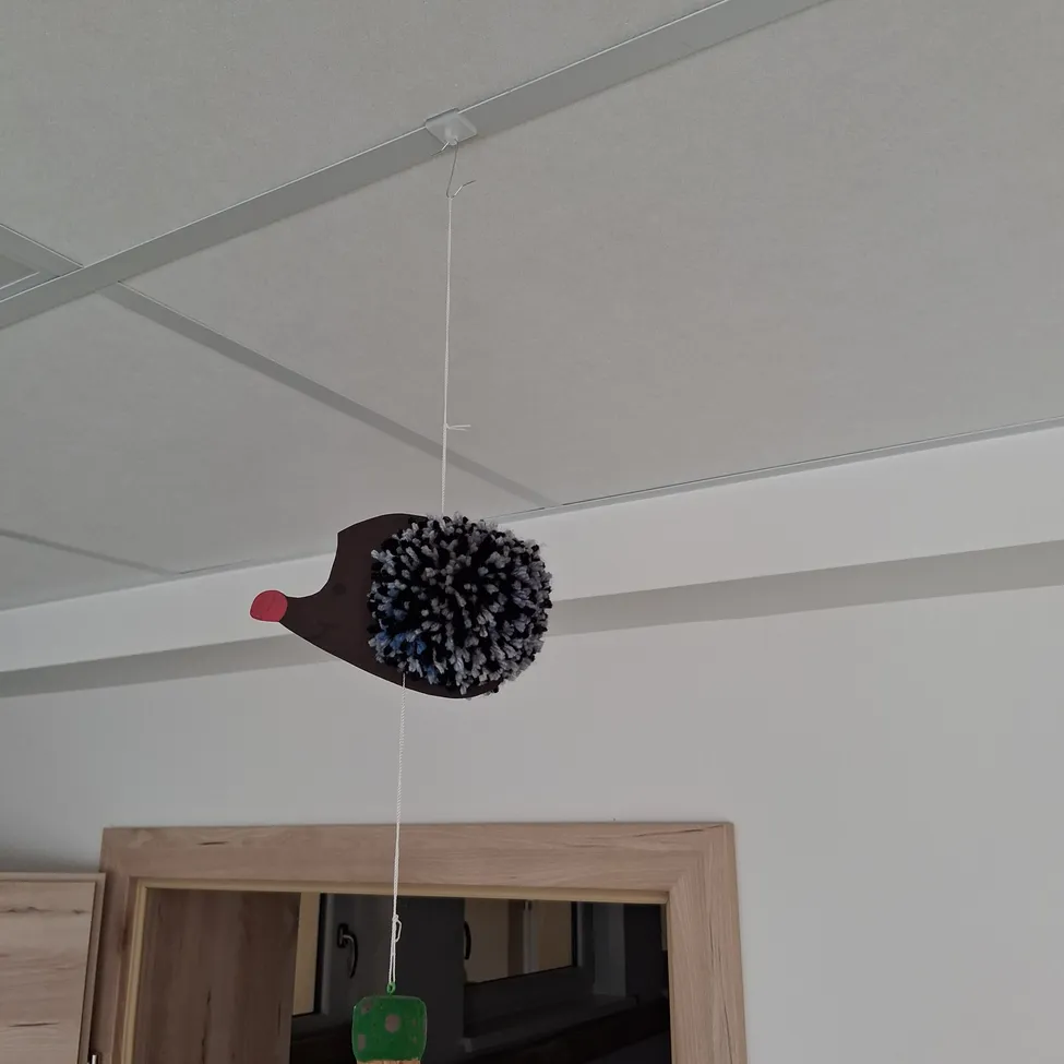 Ein vogelförmiges Objekt mit einem Pom-Pom-Schwanz hängt an der Decke.