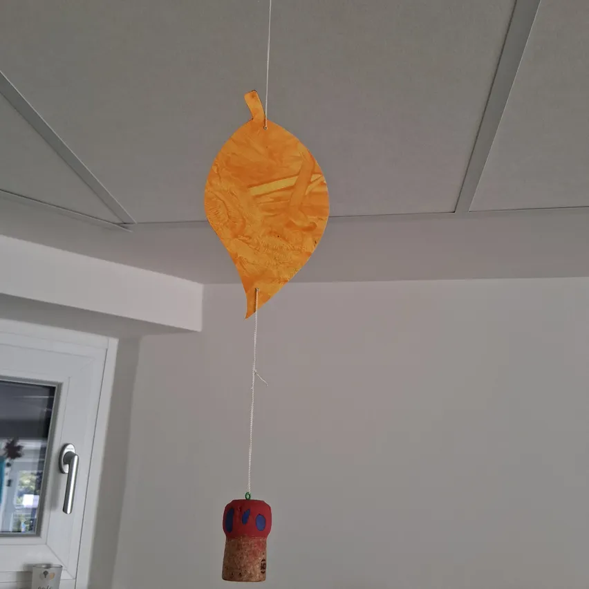 Ein orangefarbenes Blatt hängt an der Decke, befestigt an einem Korken.