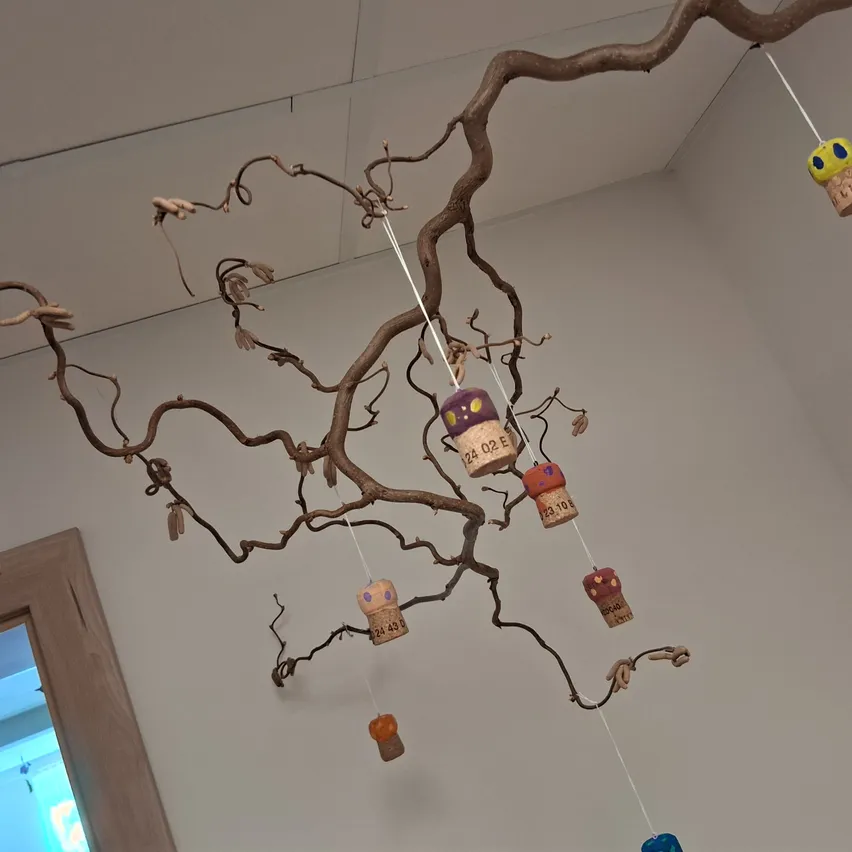 Ein Ast mit bunten Korken, die daran hängen. Die Korken sind in verschiedenen Farben und Designs bemalt.