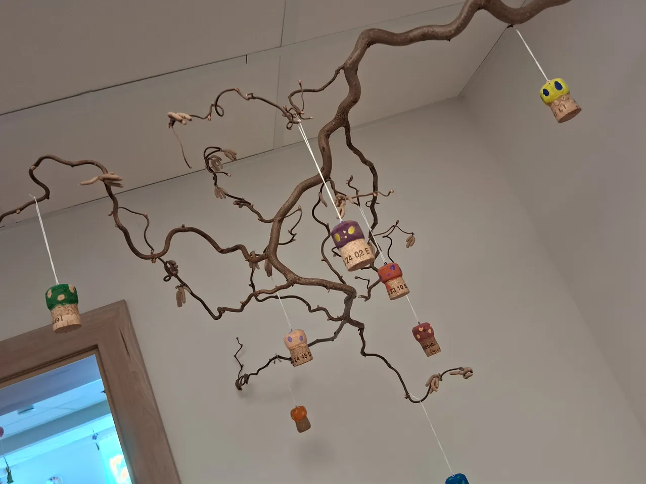 Ein Ast mit bunten Korken, die daran hängen. Die Korken sind in verschiedenen Farben und Designs bemalt.